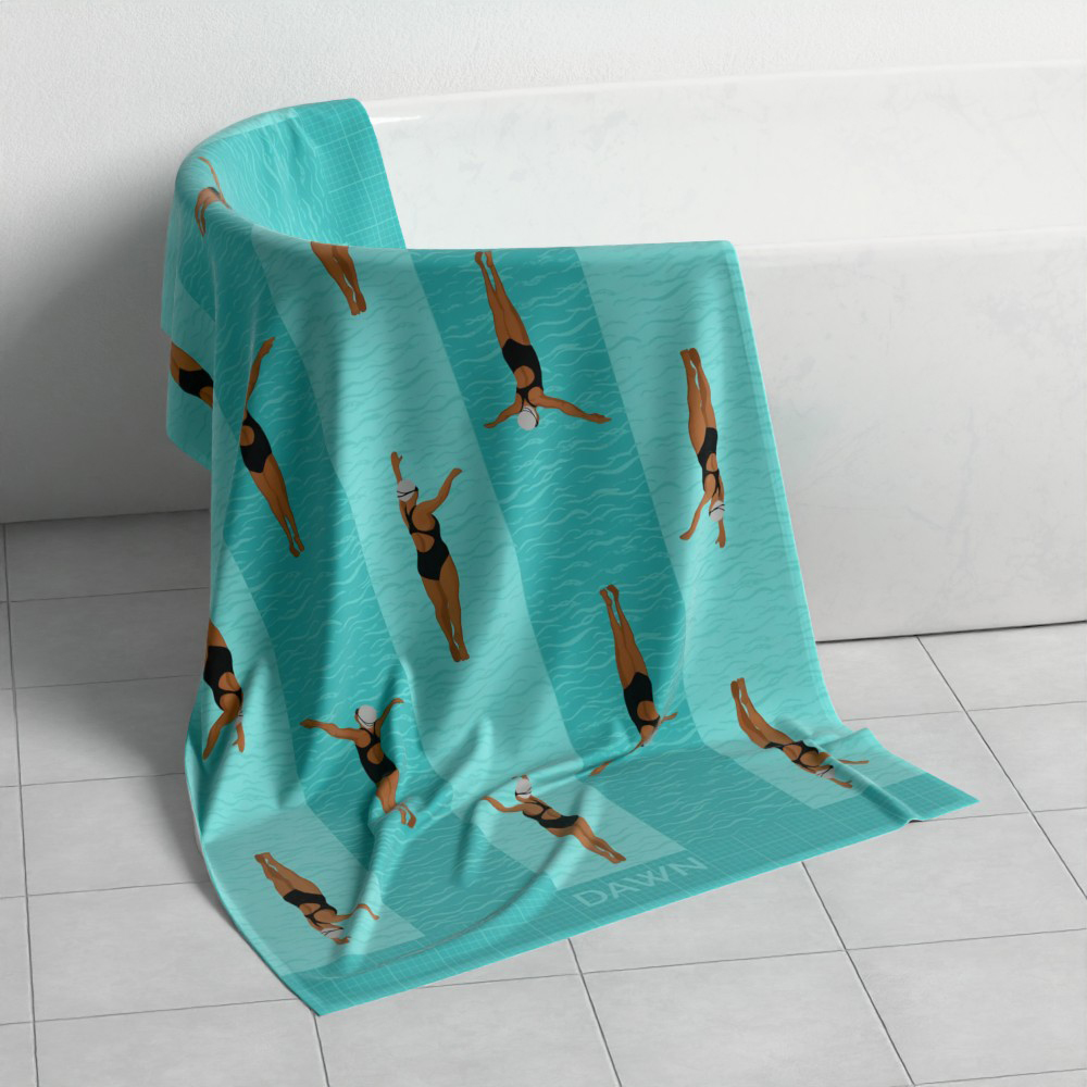 A custom swim towel draped across a bath and spilling onto white tiles. The towel has a repeat pattern of two female Indian swimmers. The towel shows custom name of Dawn.
