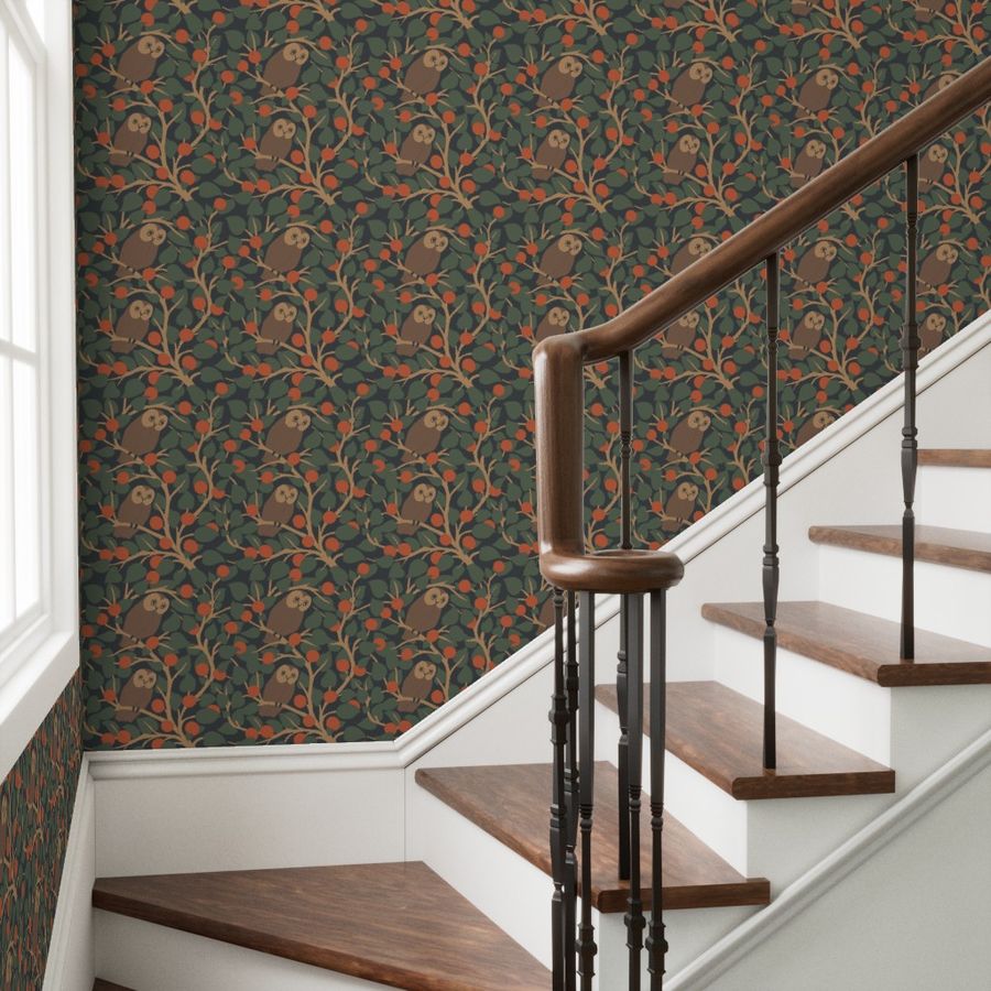 A hallway with stairs with iron spindles and a dark wooden curved banister by a side window. The wallpaper features a repeat pattern of barn owls sitting in trees with red/orange berries or fruits