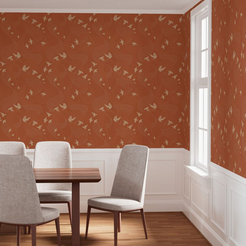 A dining room scene with cream upholstered chairs around and wooden table with a side window. The wallpaper is orange and features murmurations in swirls with close ups of white birds.